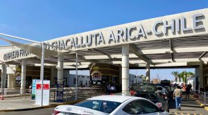 Entrada al Complejo Fronterizo Chacalluta en Arica, Chile, con vehículos y personas esperando en la fila.