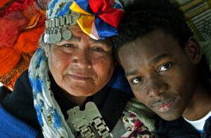 Una mujer mayor con tocado tradicional y un joven juntos, ambos con expresiones serenas.