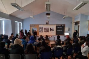 Personas reunidas en una sala con carteles y velas sobre una mesa en el frente, en un evento titulado "Los sitios de memoria".