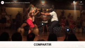 Personas bailando en un escenario con vestimenta tradicional, mientras espectadores observan.