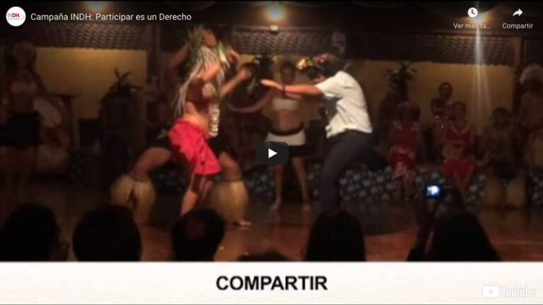 Personas bailando en un escenario con vestimenta tradicional, mientras espectadores observan.