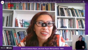 Mujer hablando en una videoconferencia con fondo de estantes llenos de libros y una ventana de interpretación en lengua de señas.