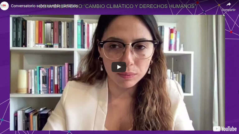 Mujer con gafas frente a una estantería de libros durante un video llamado "Conversatorio sobre cambio climático".