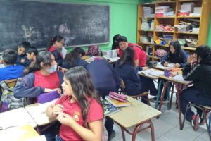 Estudiantes sentados en sus escritorios trabajando en grupo en un aula escolar.