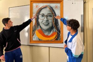 Dos personas señalando un retrato intervenido con hilos de colores y un marco dorado.