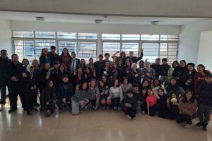 Un grupo diverso de personas posando en una habitación con ventanas grandes en el fondo.