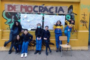 Grupo de niños frente a un mural de "DEMOCRACIA" con corazones pintados, posando frente a una pared amarilla con graffiti.