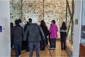 Grupo de personas observando una pared llena de pequeñas fotografías en blanco y negro en un museo.