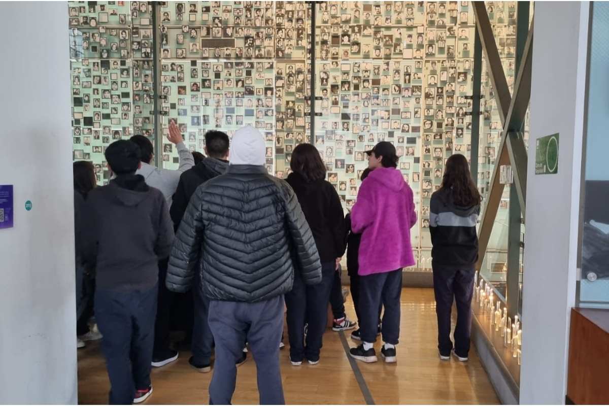 Grupo de personas observando una pared llena de pequeñas fotografías en blanco y negro en un museo.