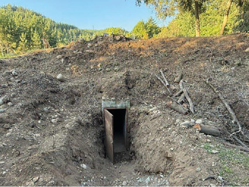 Entrada a un pequeño túnel excavado en una ladera cubierta de tierra y piedras, rodeada de vegetación y árboles en un entorno natural.