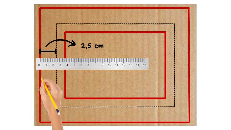 Un cartón con dos rectángulos delineados en rojo y negro, uno dentro del otro, y una regla que muestra una medida de 2,5 cm entre los bordes. Una mano sostiene un lápiz junto a la regla, aparentemente midiendo la distancia entre los rectángulos.
