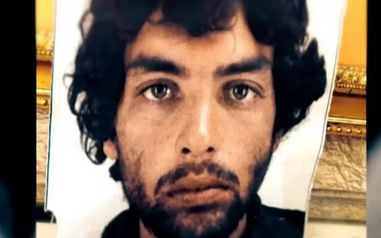 Retrato de un hombre de pelo rizado y mirada seria, con barba incipiente, sobre un fondo parcialmente visible.