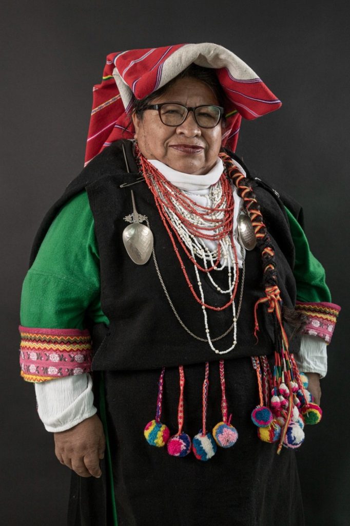 Persona vestida con traje tradicional indígena, con un tocado rojo, collares coloridos y adornos de lana.